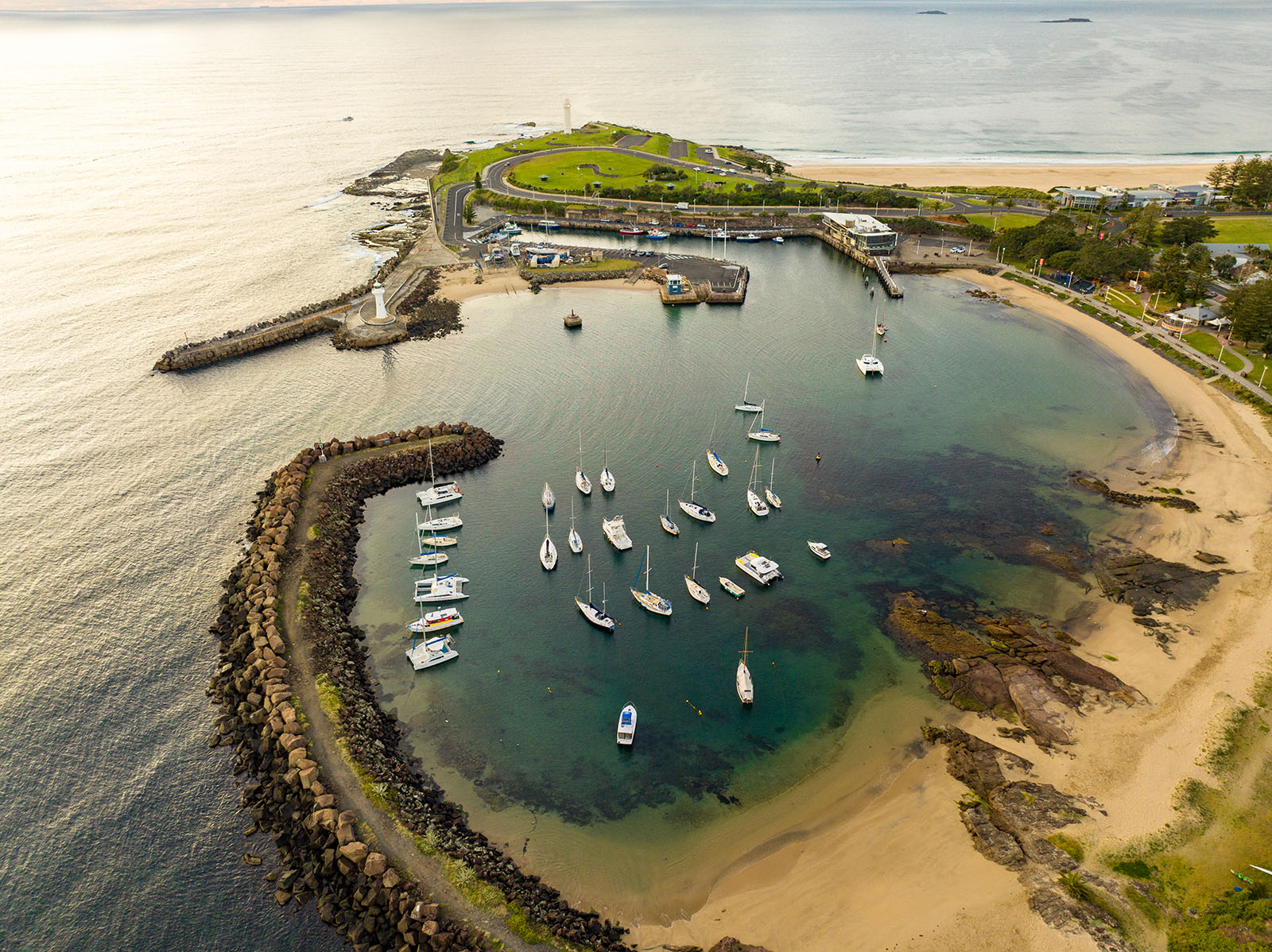 Aerial view of boats in Wollongong Harbour, with two lighthouses, breakwaters and a sandy beach.